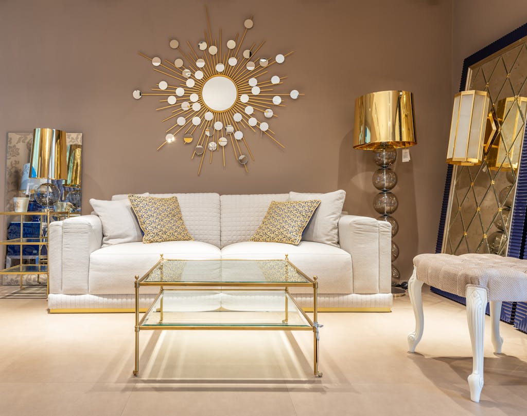 Comfortable white sofa placed near glass table at wall with decorative elements in stylish living room with mirror and table lamp